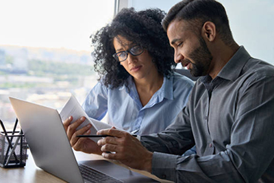 Two individuals, a woman and a man, reviewing documents together at a desk in an office.