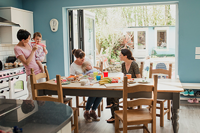 Four women and two children gathered around a table in a bright, modern kitchen with blue walls.