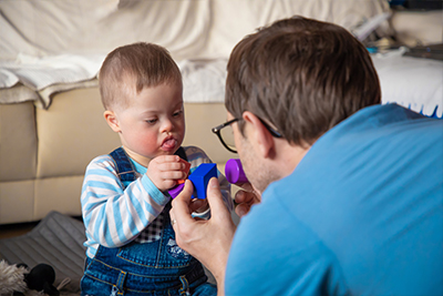 Adult male and young child interact with a blue object in a cozy living space.